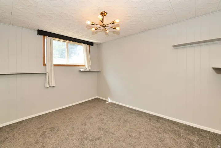 Carpeted flooring, paneled walls, window with wooden trim, built-in shelving, and a decorative ceiling light fixture