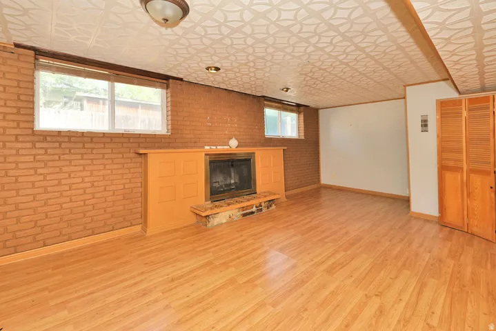 Wood-finish flooring, brick accent wall, fireplace with stone hearth, built-in wooden cabinetry, and patterned ceiling panels