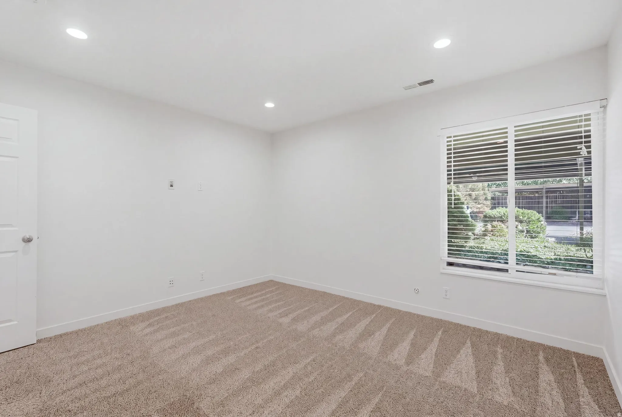 Recessed lighting, textured carpeting, crisp white walls, white window blinds, and a white interior door