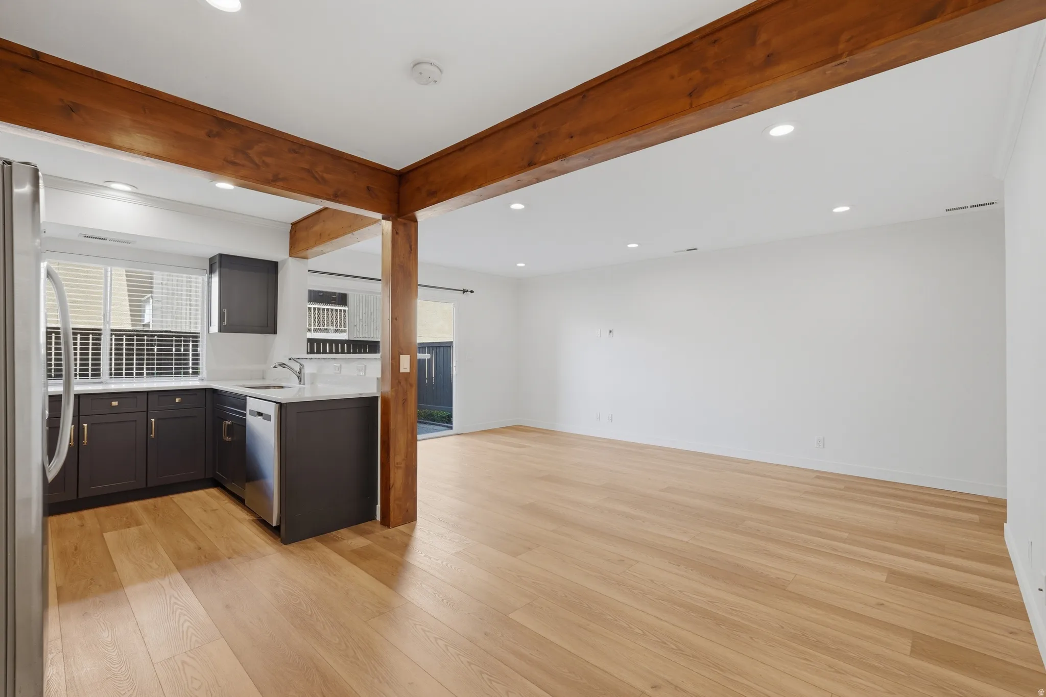 Open-concept living area with wood-finish flooring, exposed wood beams, recessed lighting, and a sliding glass door