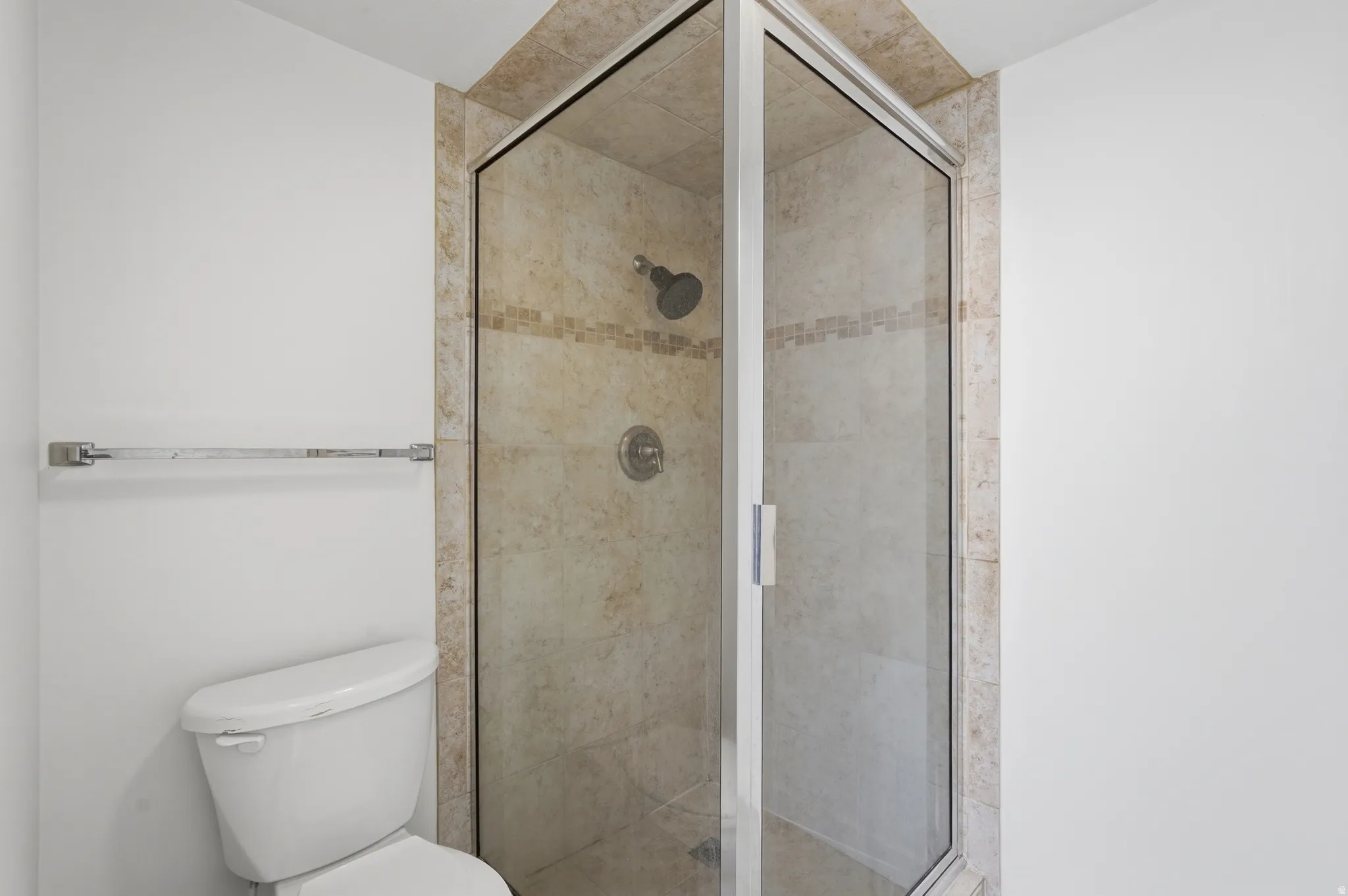 Glass-enclosed shower with tiled walls and chrome fixtures