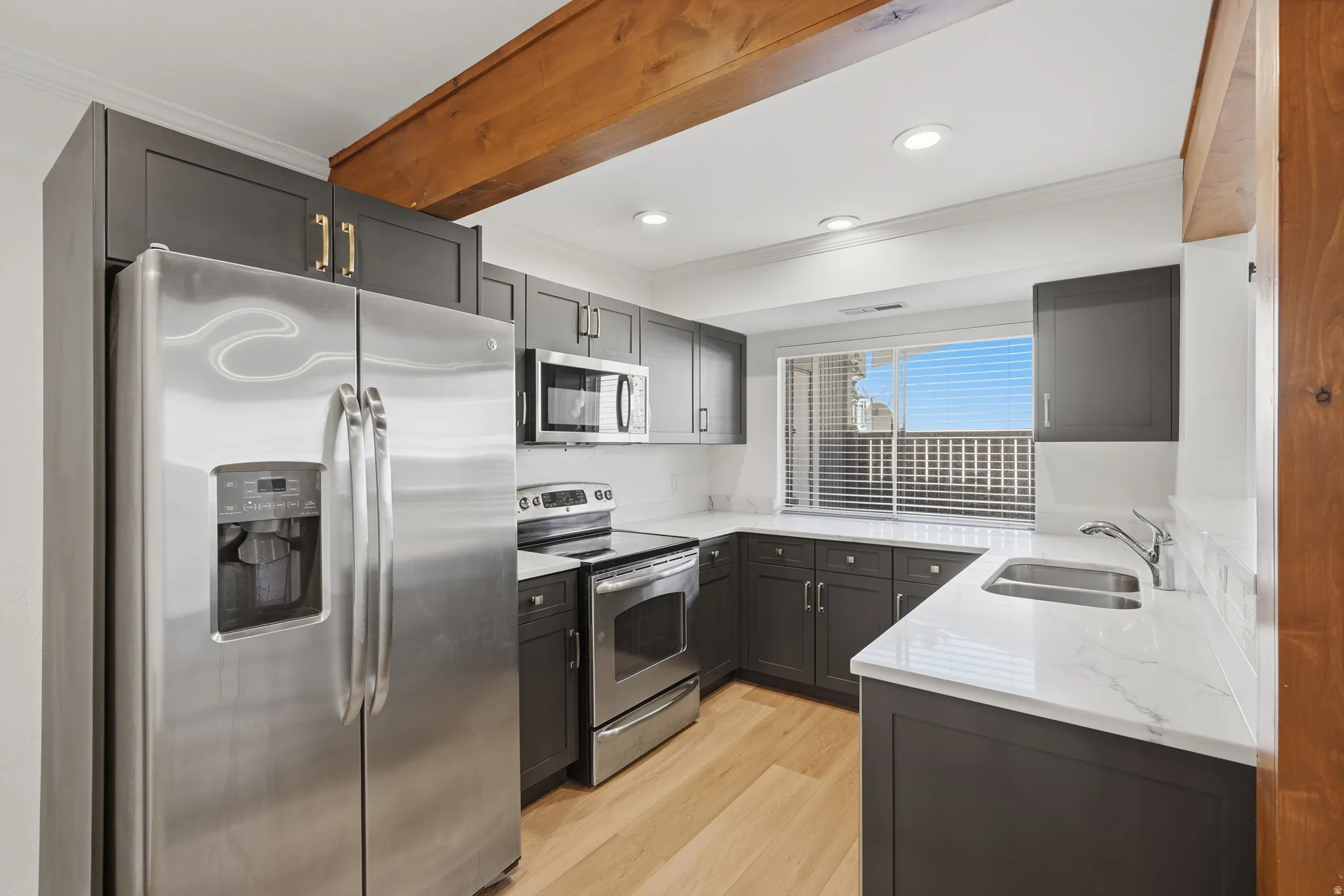 Modern kitchen featuring dark cabinetry, stainless steel appliances, light wood-finish flooring, and white countertops