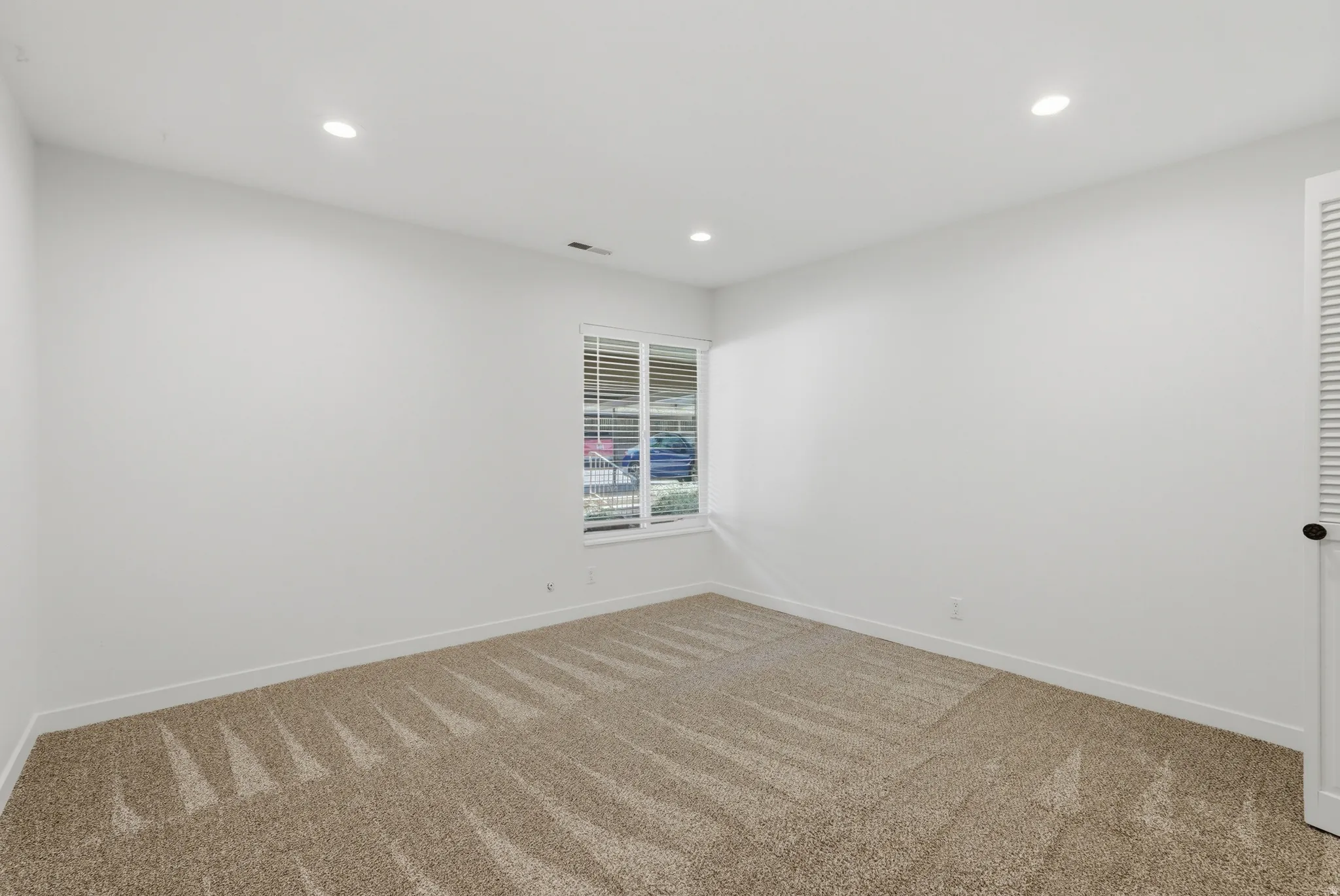 Recessed ceiling lighting, window with blinds, neutral wall paint, textured carpeting, louvered door