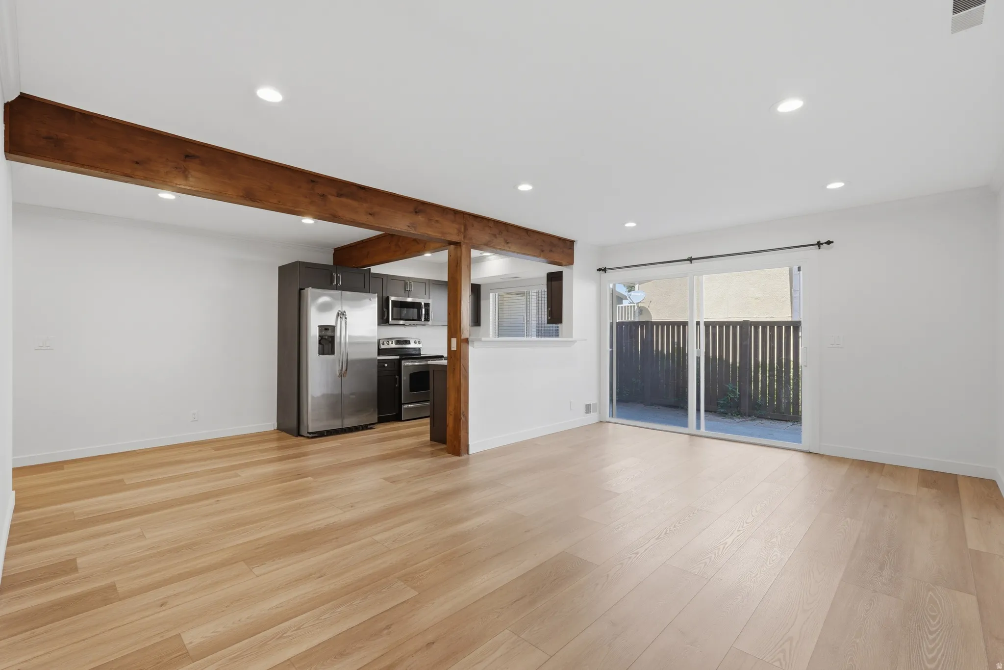 Open-concept living area with wood-finish flooring, exposed ceiling beams, recessed lighting, and a kitchen featuring stainless steel appliances