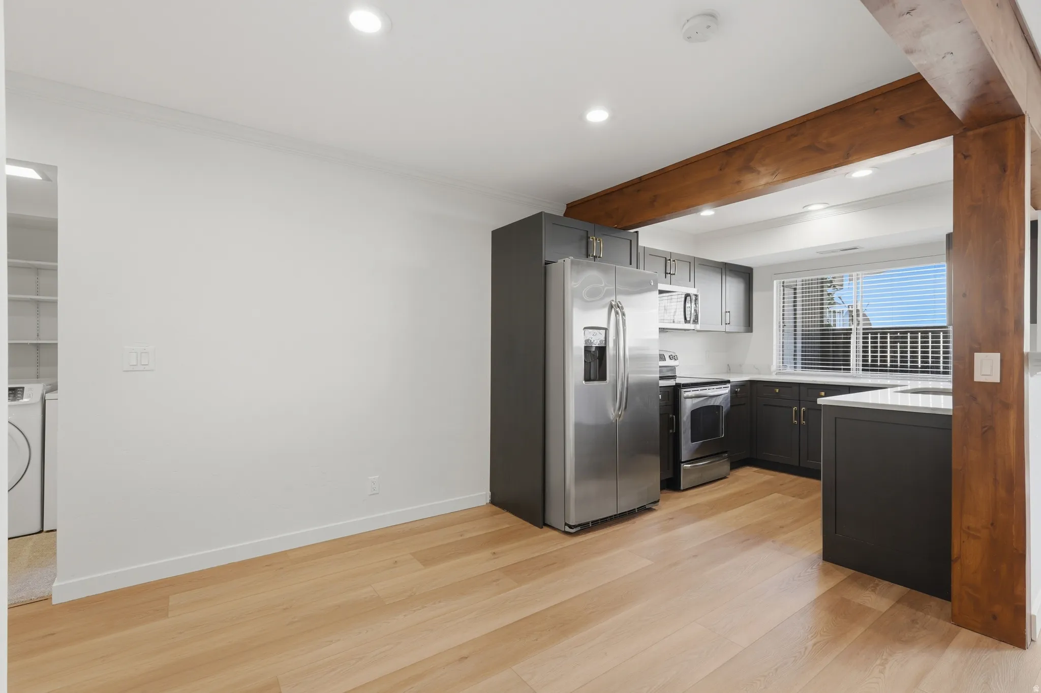 Kitchen with dark cabinetry, stainless steel appliances, light countertops, and wood-finish flooring