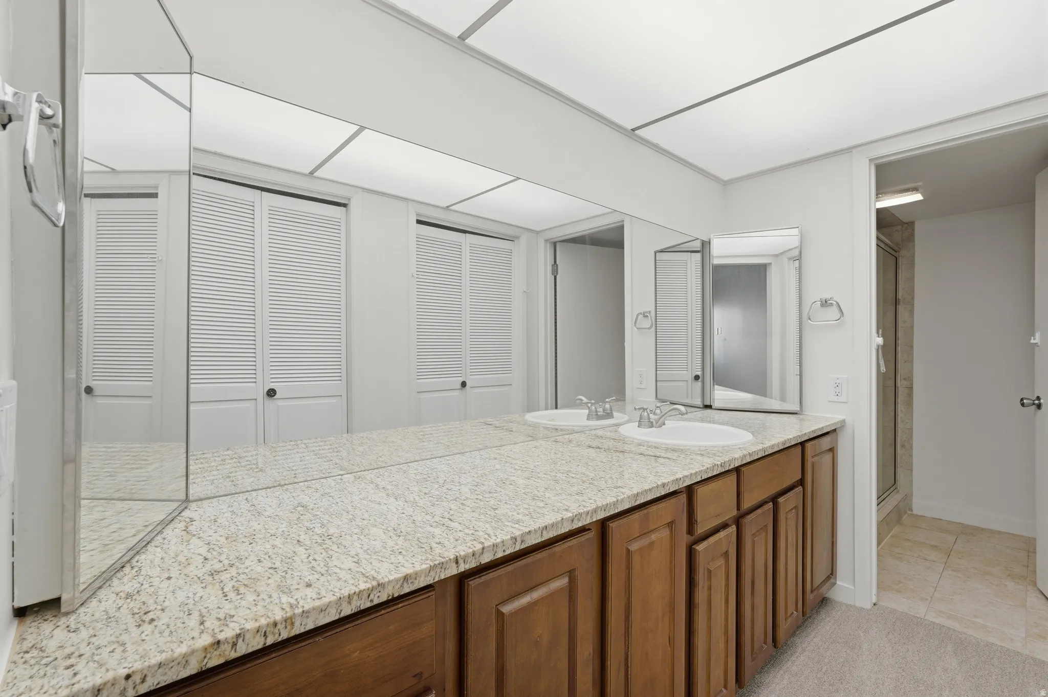 Dual vanity with granite countertop, integrated sinks, wood-finish cabinetry, and a full-wall mirror