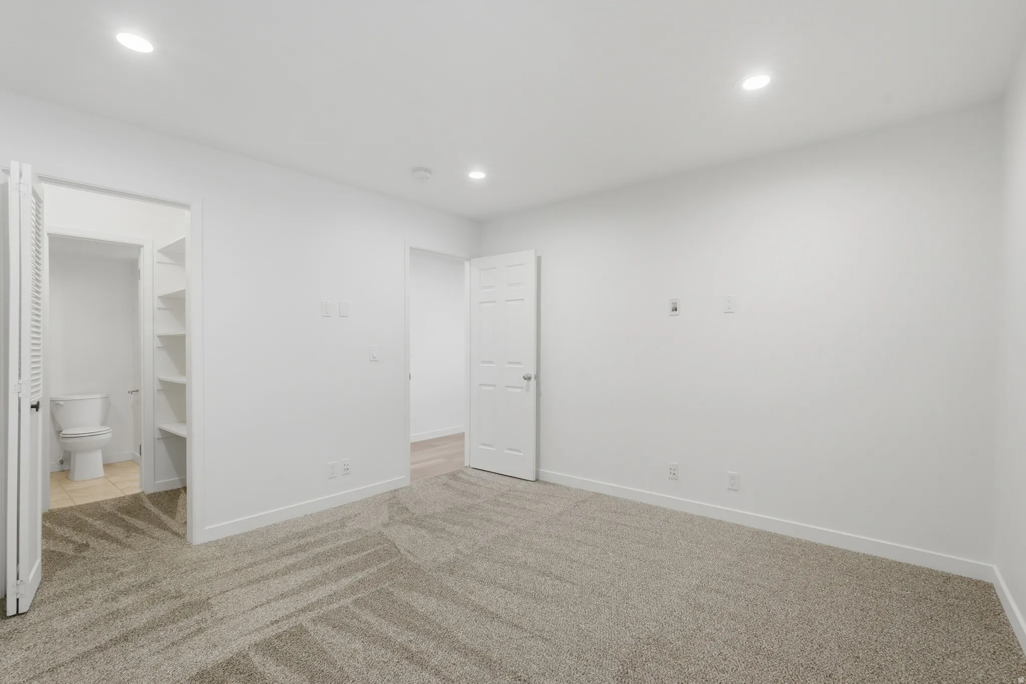 Recessed ceiling lighting, white walls, and soft gray carpet flooring