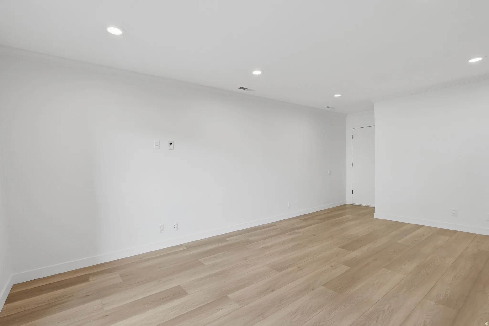 Recessed lighting illuminates the expansive room featuring wood-finish flooring and white walls