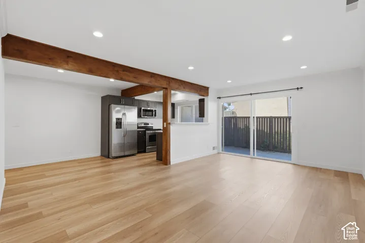 Open-concept living area with wood-finish flooring, exposed ceiling beams, recessed lighting, and a kitchen featuring stainless steel appliances