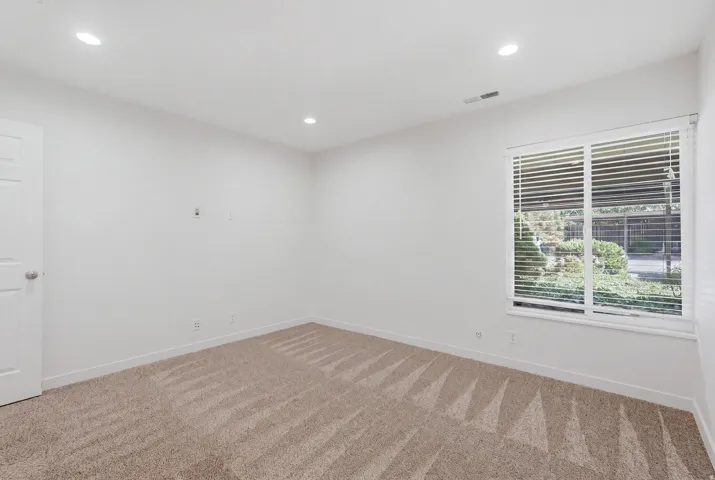 Recessed lighting, textured carpeting, crisp white walls, white window blinds, and a white interior door