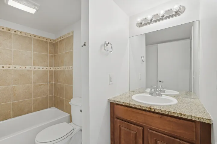 Bathroom with a tiled tub/shower combination, white toilet, and a vanity featuring a granite-style countertop, undermount sink, and wood-finish cabinetry
