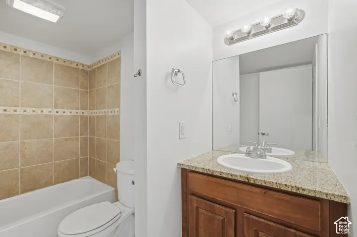 Bathroom with a tiled tub/shower combination, white toilet, and a vanity featuring a granite-style countertop, undermount sink, and wood-finish cabinetry