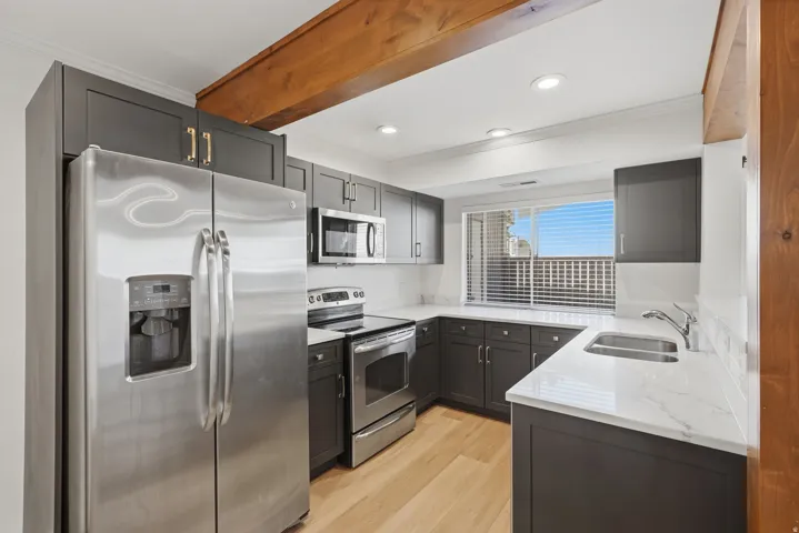 Modern kitchen featuring dark cabinetry, stainless steel appliances, light wood-finish flooring, and white countertops