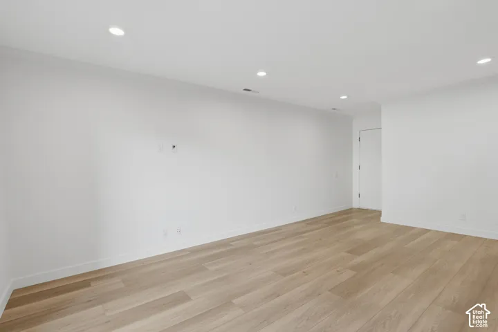 Recessed lighting illuminates the expansive room featuring wood-finish flooring and white walls