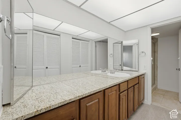 Dual vanity with granite countertop, integrated sinks, wood-finish cabinetry, and a full-wall mirror