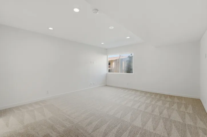 Recessed lighting illuminates a spacious room featuring a window and patterned carpeting