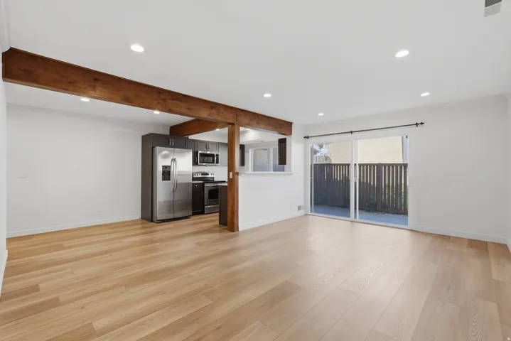 Open-concept living area with wood-finish flooring, exposed ceiling beams, recessed lighting, and a kitchen featuring stainless steel appliances