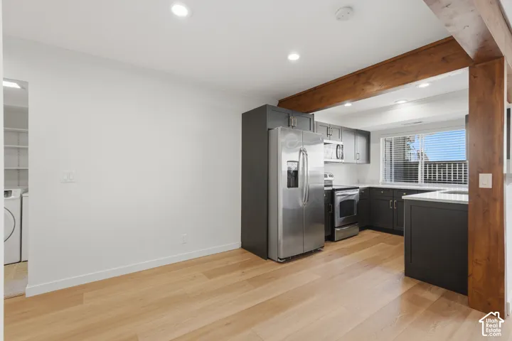 Kitchen with dark cabinetry, stainless steel appliances, light countertops, and wood-finish flooring