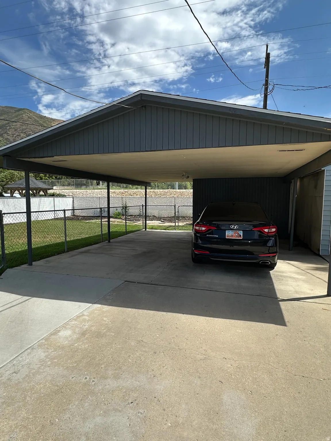 Covered carport providing sheltered parking, featuring a concrete surface and a partial chain-link fence