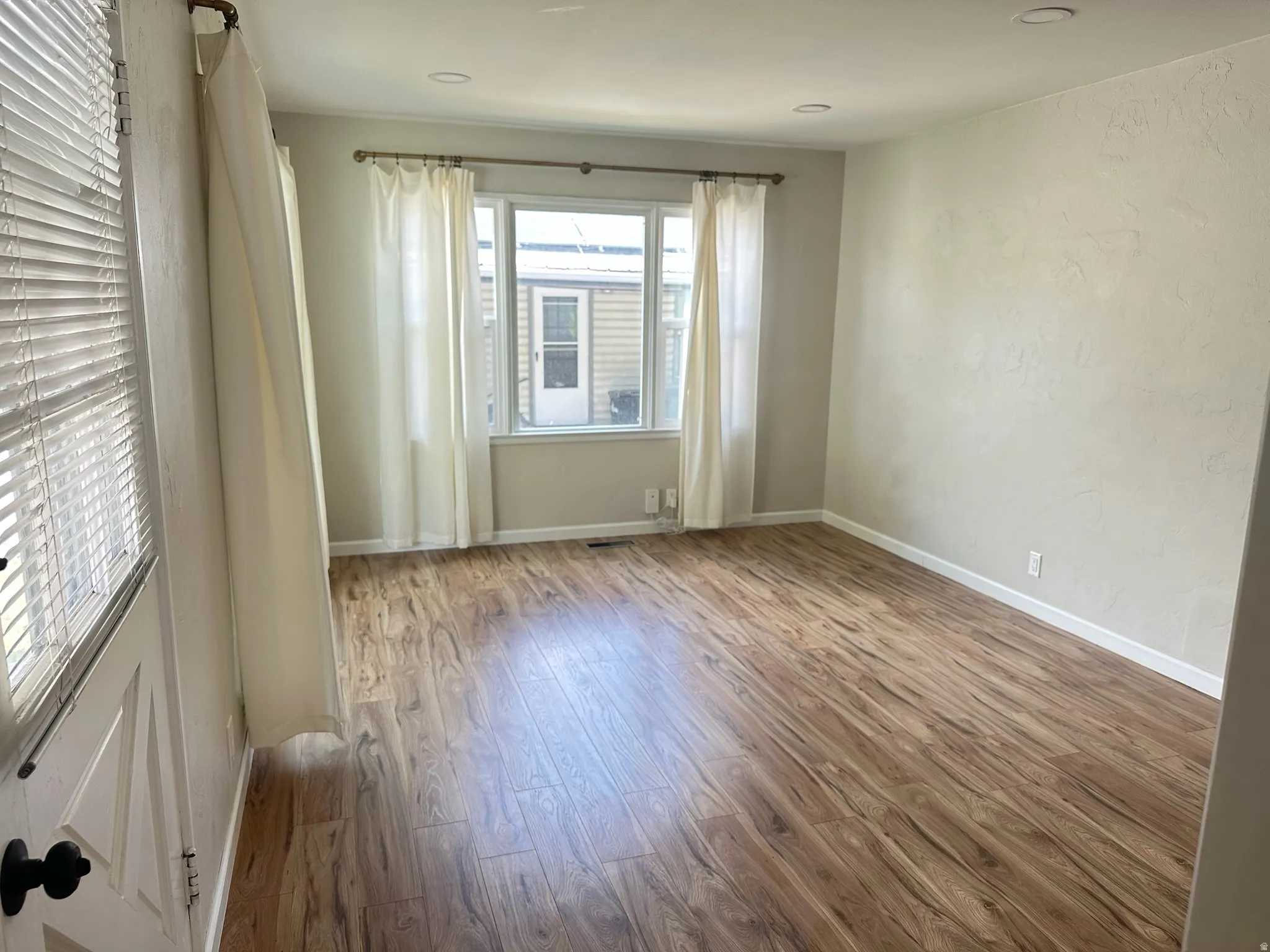 Wood-finish flooring throughout, featuring a window with blinds and curtains
