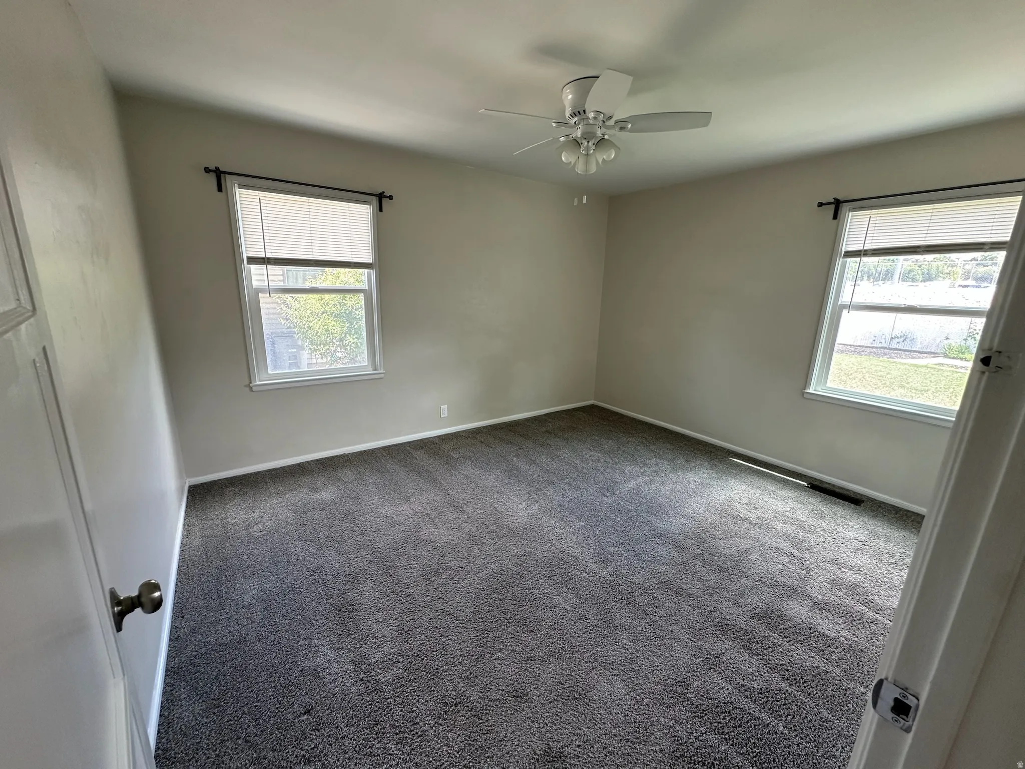 Neutral paint palette, dark gray carpeting, ceiling fan with integrated lighting, and two windows with blinds