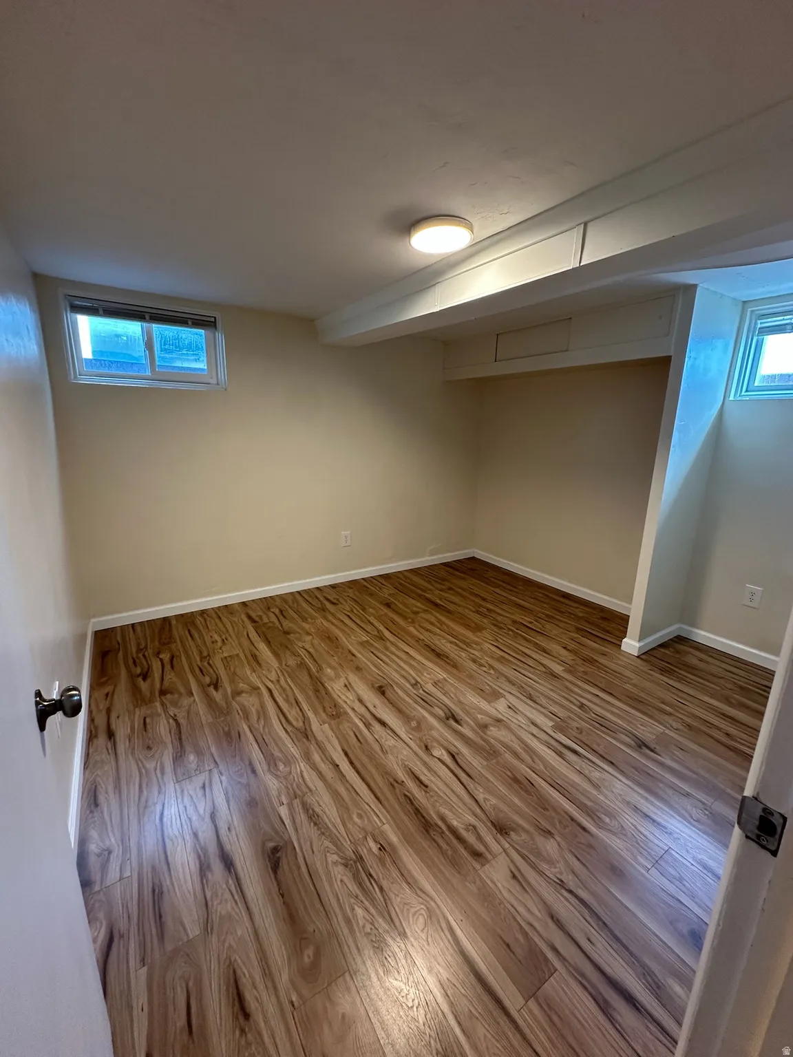Wood-finish flooring with white baseboards, recessed window, and flush-mount ceiling light