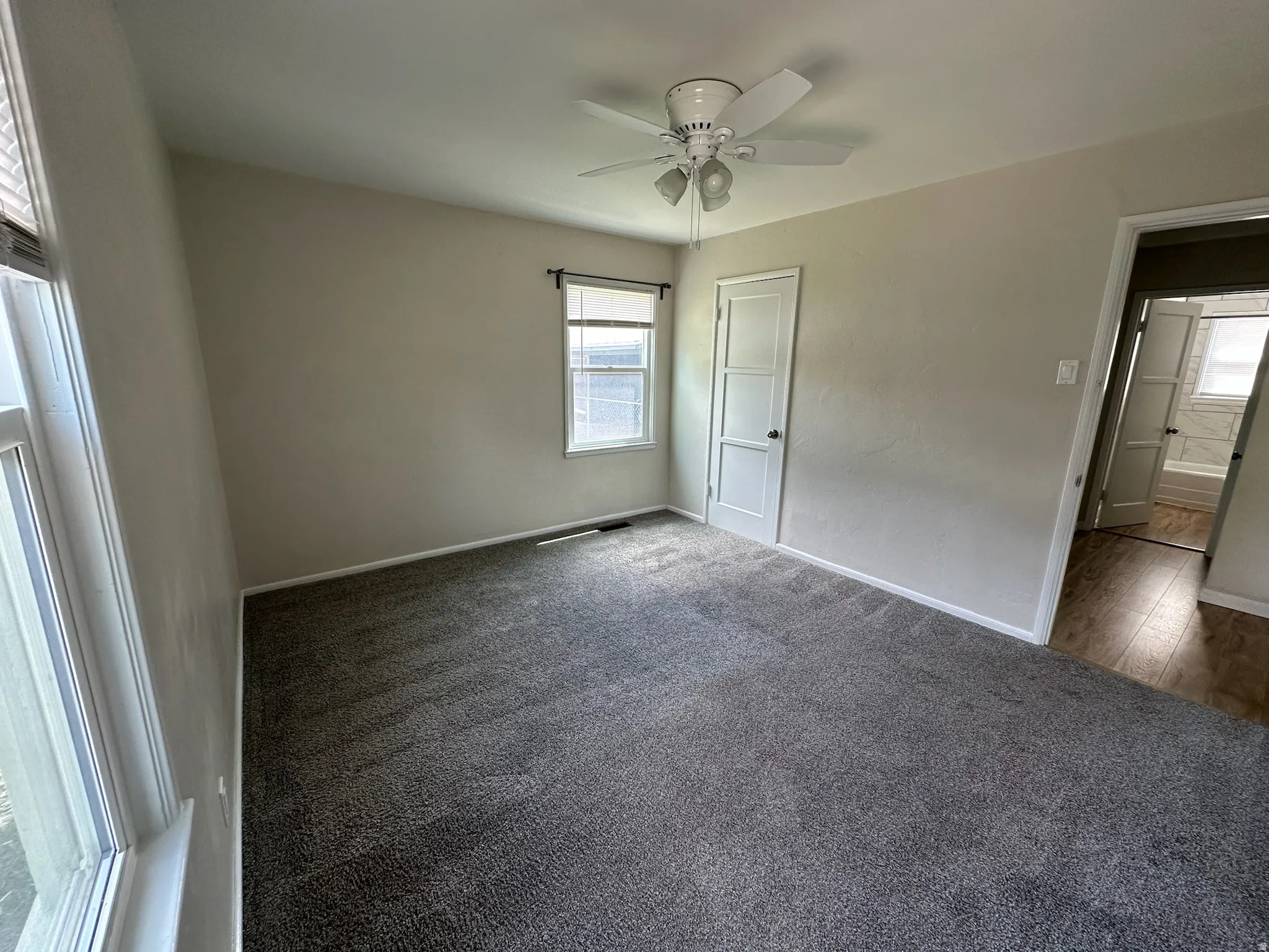Neutral wall tones, grey carpeting, a multi-paneled door, and a ceiling fan