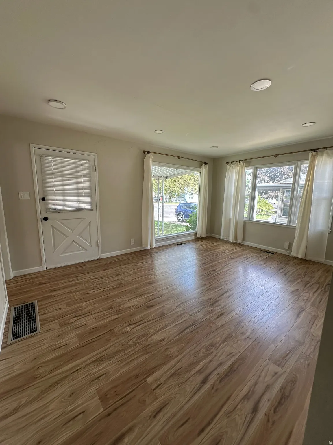 Recessed ceiling lighting, wood-finish flooring, multiple windows, and a white paneled door