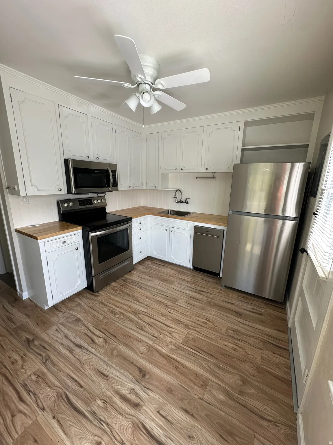 Kitchen featuring white cabinetry, wood-finish countertops, wood-finish flooring, stainless steel appliances, and a ceiling fan