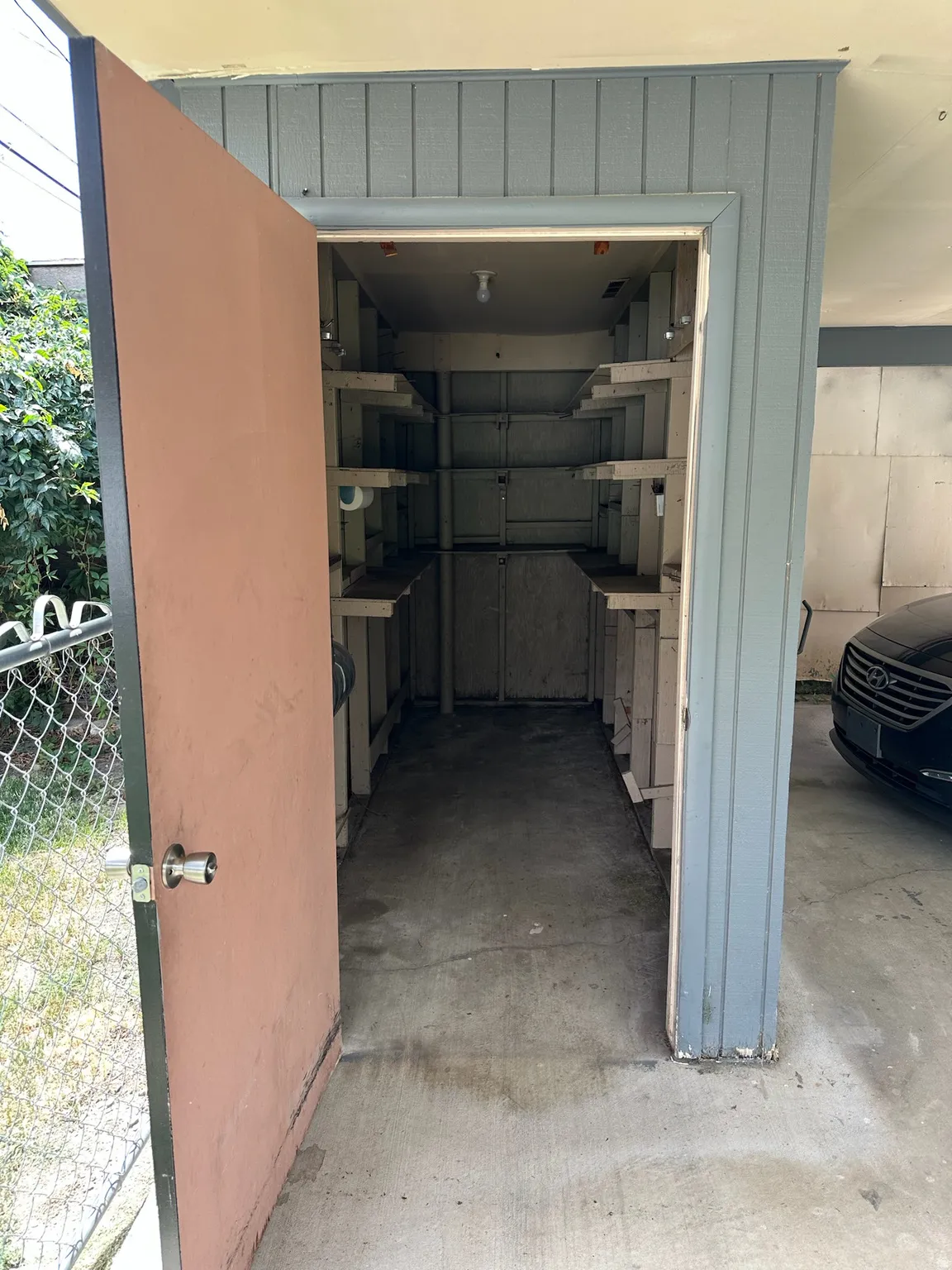Storage shed with built-in shelving, concrete flooring, and an exterior wood-paneled wall