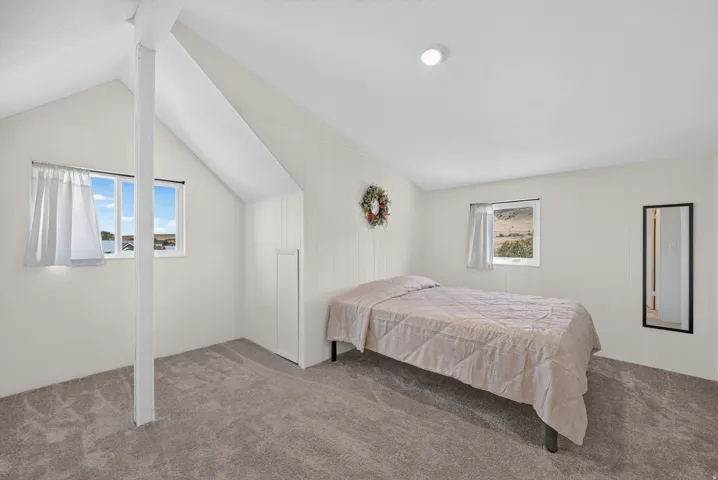 Vaulted ceiling with exposed beam, recessed lighting, two windows, wall paneling, and gray carpet flooring