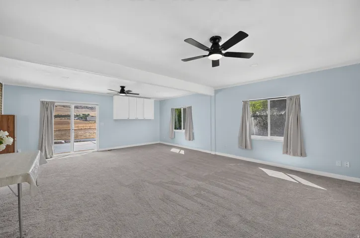 Spacious room featuring light blue walls, gray carpet flooring, dual ceiling fans, and multiple windows