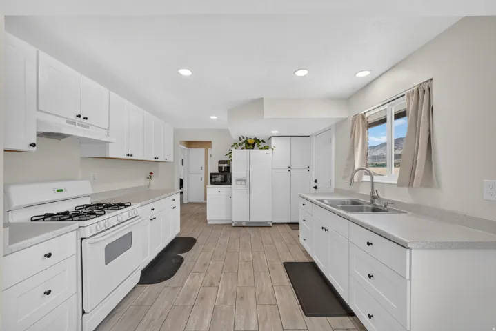 Kitchen featuring white shaker cabinetry, light-toned countertops, wood-finish flooring, a double basin stainless steel sink, and recessed lighting