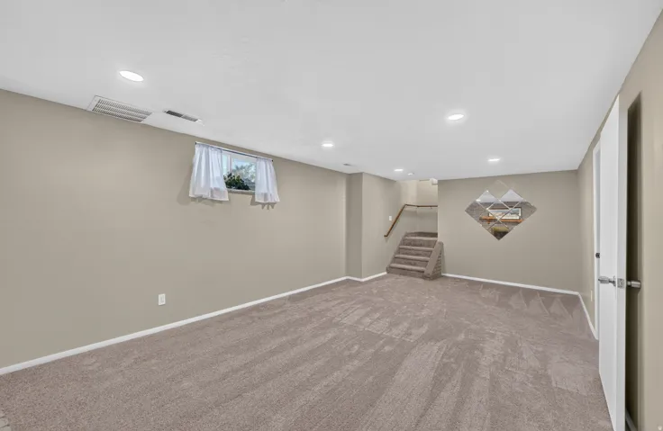 Carpeted flooring, recessed lighting, neutral wall paint, and a staircase with a wood-finish handrail