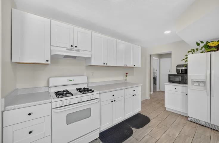 White cabinetry with black hardware, light-toned countertops, white range oven, and wood-finish tile flooring