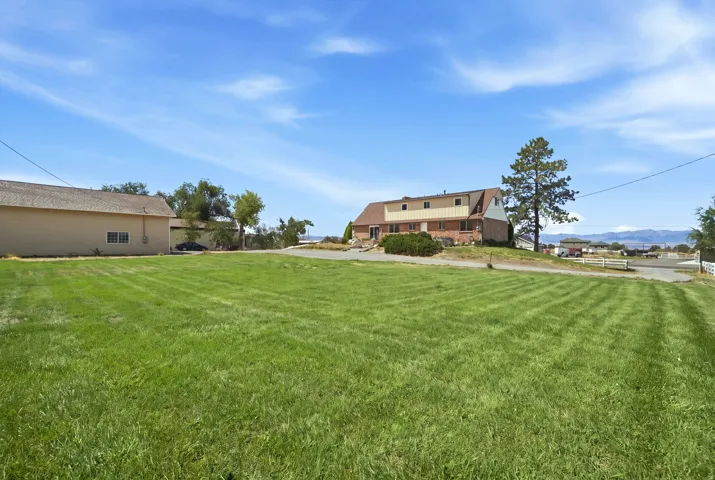 Expansive green lawn with a large residence featuring brick and siding exterior, a separate auxiliary structure, and established landscaping