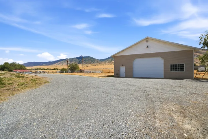 Gravel driveway leading to a large building featuring a roll-up garage door, multiple windows, and a pedestrian entry door