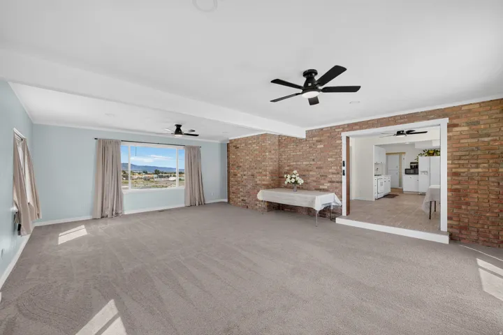 Carpeted living area with exposed brick accents, large picture window, and ceiling fans