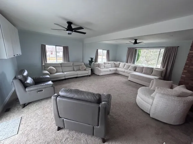 Spacious room featuring carpeting, multiple windows, exposed brick accent, and ceiling fans