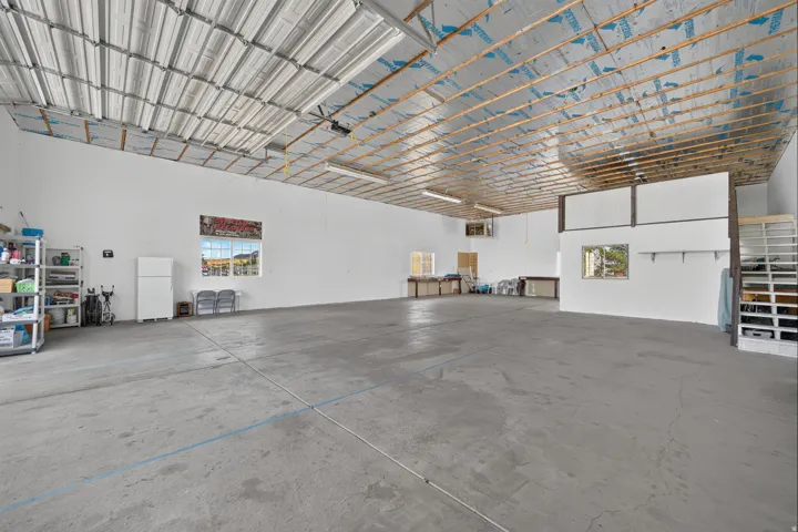 Spacious concrete flooring, high metal ceiling, multiple windows, built-in shelving, and a partial upper-level structure