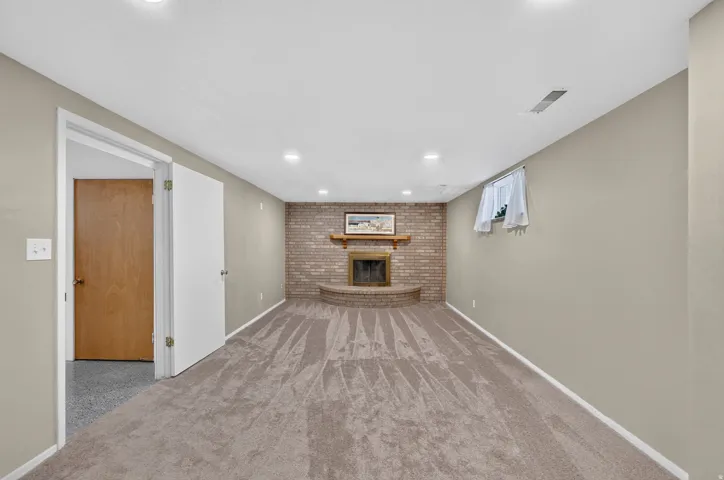Recessed lighting throughout, brick fireplace with raised hearth, light-toned carpeting, neutral wall paint, and white trim