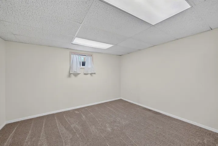 Recessed fluorescent lighting, drop ceiling, neutral carpeting, light-toned wall paint, and a window with white trim