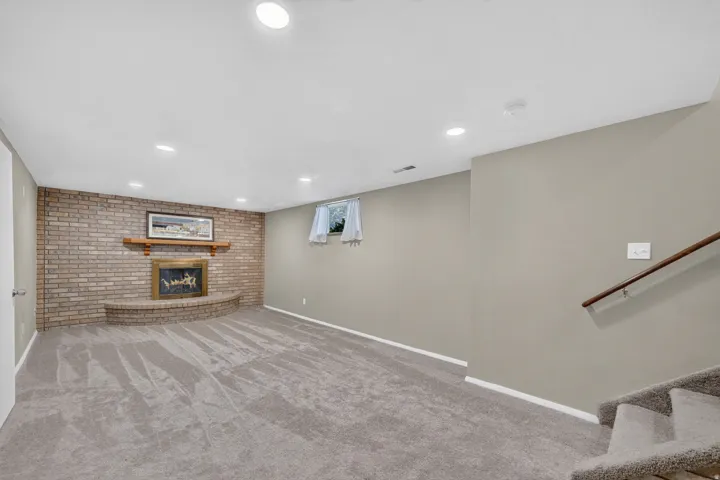 Recessed lighting, brick accent wall, wood mantle, built-in fireplace, and carpeted flooring