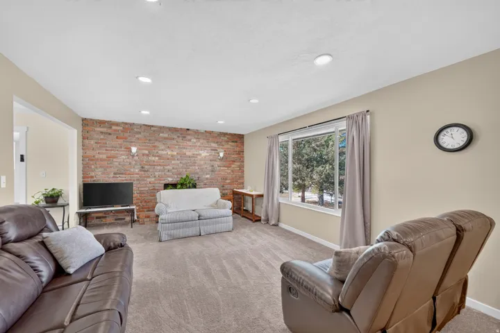 Spacious living area featuring a prominent exposed brick accent wall, recessed lighting, and soft carpeting