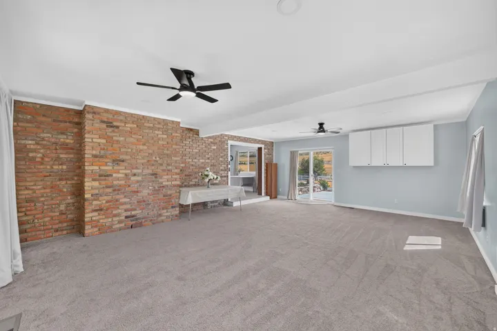Exposed brick wall, light gray carpeting, ceiling fans, built-in white cabinetry, and sliding glass doors