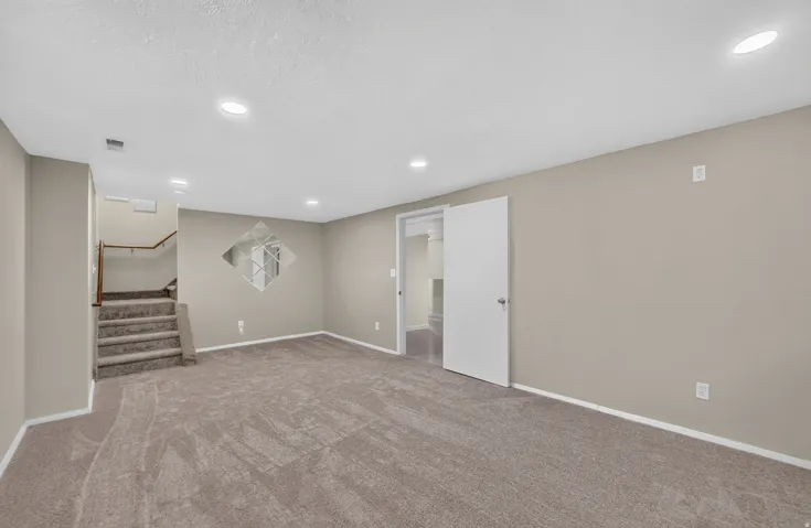 Spacious basement recreation area featuring plush carpeting, recessed lighting, and multiple white interior doors providing access to adjoining spaces