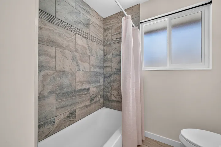 Bathtub with tile surround, mosaic accent band, and white-framed window