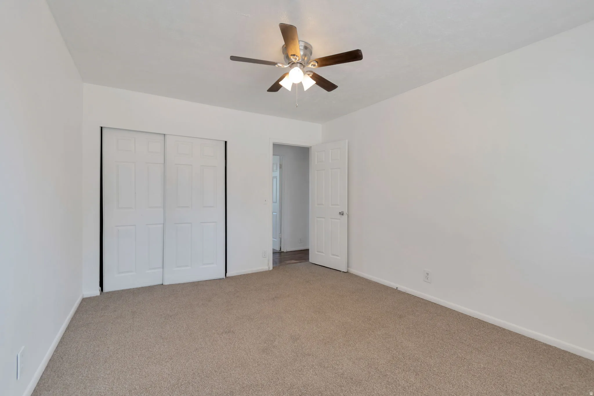 Neutral wall tones, ceiling fan with light fixture, textured carpet flooring, and white paneled bi-fold closet doors