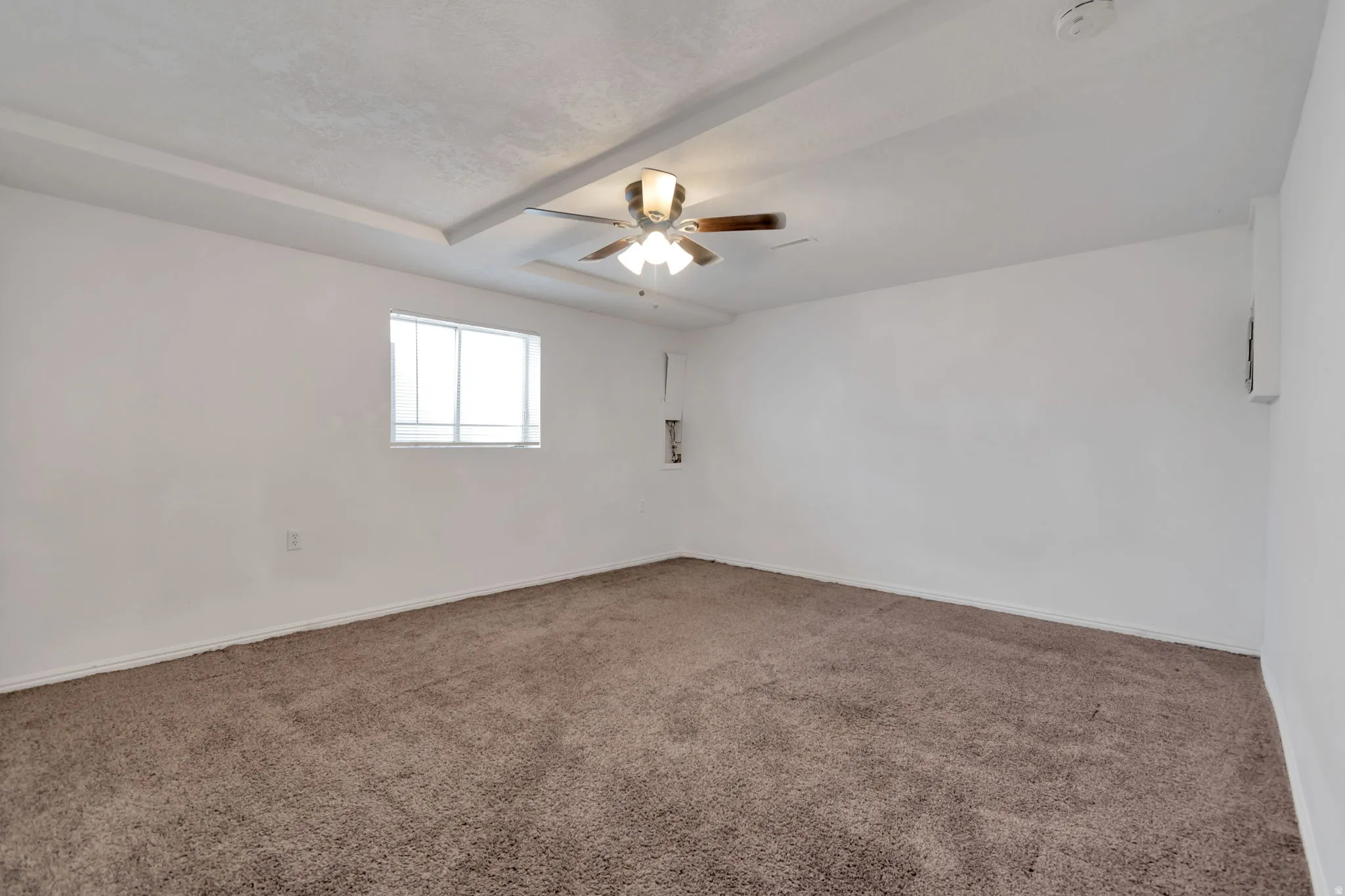 Recessed tray ceiling with a built-in ceiling fan, white walls, and carpeting