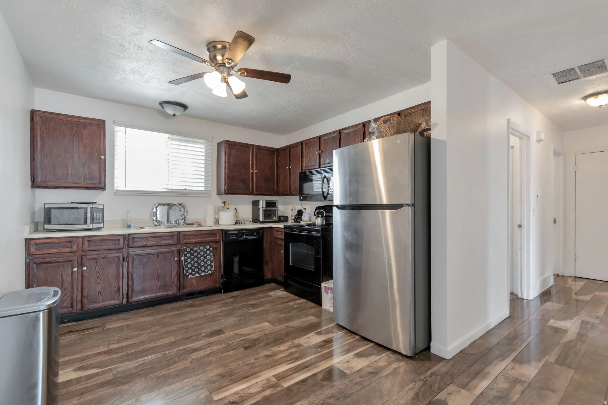 Kitchen featuring wood-finish flooring, rich wood cabinetry, a ceiling fan with integrated lighting, and a window with horizontal blinds